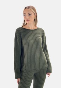 Sweter z długim rękawem w ciemnozielonym kolorze, wykonany z materiału o fakturowanym splocie. Posiada szeroki dekolt i luźny krój. Połączony z pasującymi spodniami.
