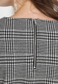 Svart och vit mönstrad klänning med en strukturmässig hundtandsdesign, som har en silvrig dragkedjestängning vid bakre halsringningen.