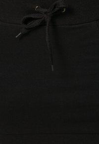 Tissu noir avec un cordon de serrage noué en un nœud, comportant des œillets en métal à la taille d'un pantalon ou d'un short.