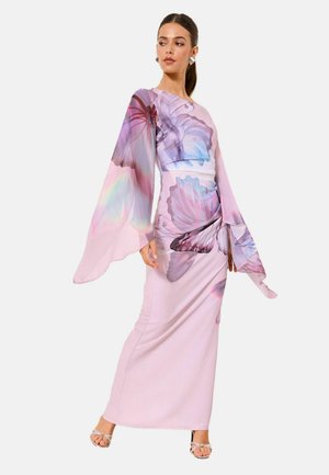 Kvinde iført en lang, lyserød kjole med store lilla og blå sommerfugleprint og brede, flagrende ærmer, der poserer med det ene ben fremad.