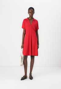 Robe rouge à manches courtes avec un col en V et une coupe décontractée, fabriquée en tissu lisse. Associée à un sac blanc et des ballerines noires.