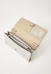 Portefeuille beige avec un extérieur texturé crème. Dispose d'une fermeture à pression, de fentes pour cartes et d'un compartiment zippé pour les pièces de monnaie ou les petits objets.