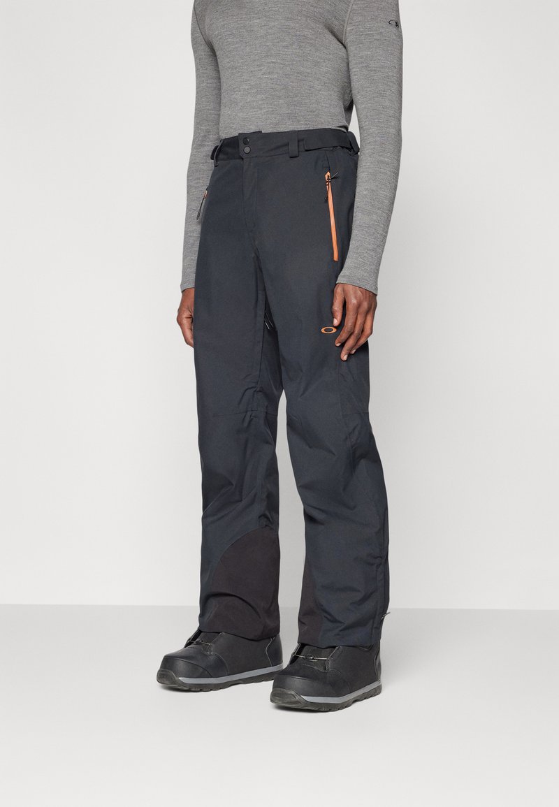 Black waterproof ski pants with an orange zipper pocket, feature a straight cut and reinforced lower sections for durability and functionality.