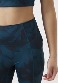 Leggings a vita alta di colore verde scuro, con un motivo a spirale. Realizzati in materiale elasticizzato con una texture liscia e cuciture piatte.
