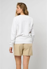 Balta džemperis ar ribotām piedurknēm un apakšmalu, pārī ar gaiši pelēkiem šortiem. Redzama gluda auduma virsma; vienkāršs, ikdienišķs dizains.