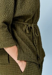 Oliven grøn tekstureret top med en bånd i taljen, der har ærmer til albuen og en afslappet pasform; parret med lignende teksturerede bukser.