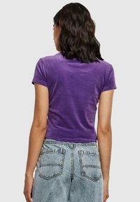 Paarse fluwelen top met korte mouwen en een cropped ontwerp, gecombineerd met lichtgewassen denim jeans met achterzakken en een vervaagde textuur.