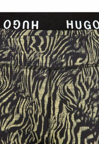 Leggings a righe nere e gialle con un motivo a strisce di tigre e una cintura elastica nera con il logo "HUGO".