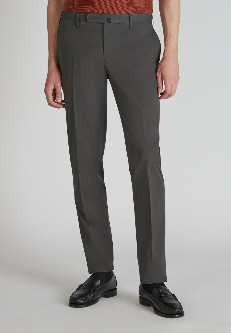 Pantaloni eleganti grigi scuri con vestibilità slim, dotati di tasche frontali, passanti per cintura e una texture di tessuto liscia. Indossati con scarpe di pelle nere.