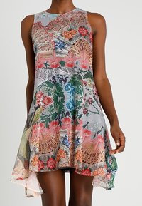 Blumenkleid aus transparenter Stoff mit asymmetrischem Saum. Es zeichnet sich durch lebendige Muster von Blumen und Spitze in einer Mischung aus Pastellfarben aus.