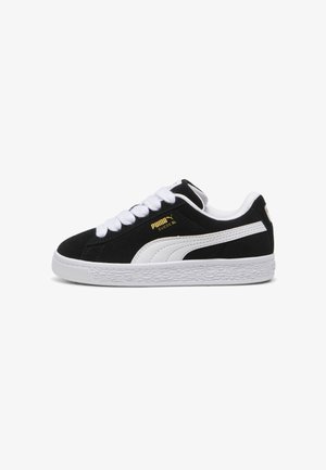Schwarze Wildledersneaker mit weißen Akzenten, flachen Schnürsenkeln, strukturierten Gummisohlen und goldenen Logodetails an der Seite. Klassisches Low-Top-Design.