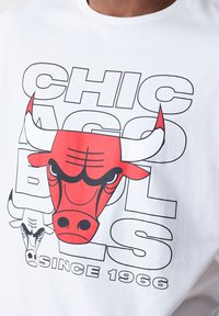 Bijela majica kratkih rukava s crvenim i crnim grafikom Chicago Bulls, velikim dizajnom glave bika i natpisom "CHICAGO BULLS OD 1966."