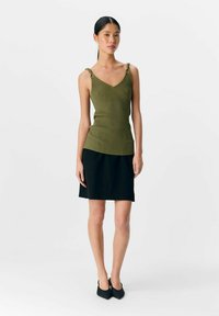 Top de canalé verde oliva con escote en V y detalles decorativos de tirantes, combinado con una falda negra de corte A y tacones negros en punta.