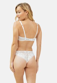 Ensemble de lingerie en dentelle blanc comprenant un string et un bralette, mettant en valeur des panneaux en mesh transparent, des bretelles réglables et une délicate bordure en dentelle florale sur les bords.