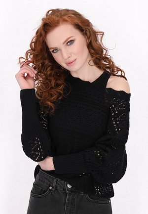 Pull en maille noire avec un design en tricot ouvert, des manches larges et une coupe décolletée. Associé à un jean sombre.