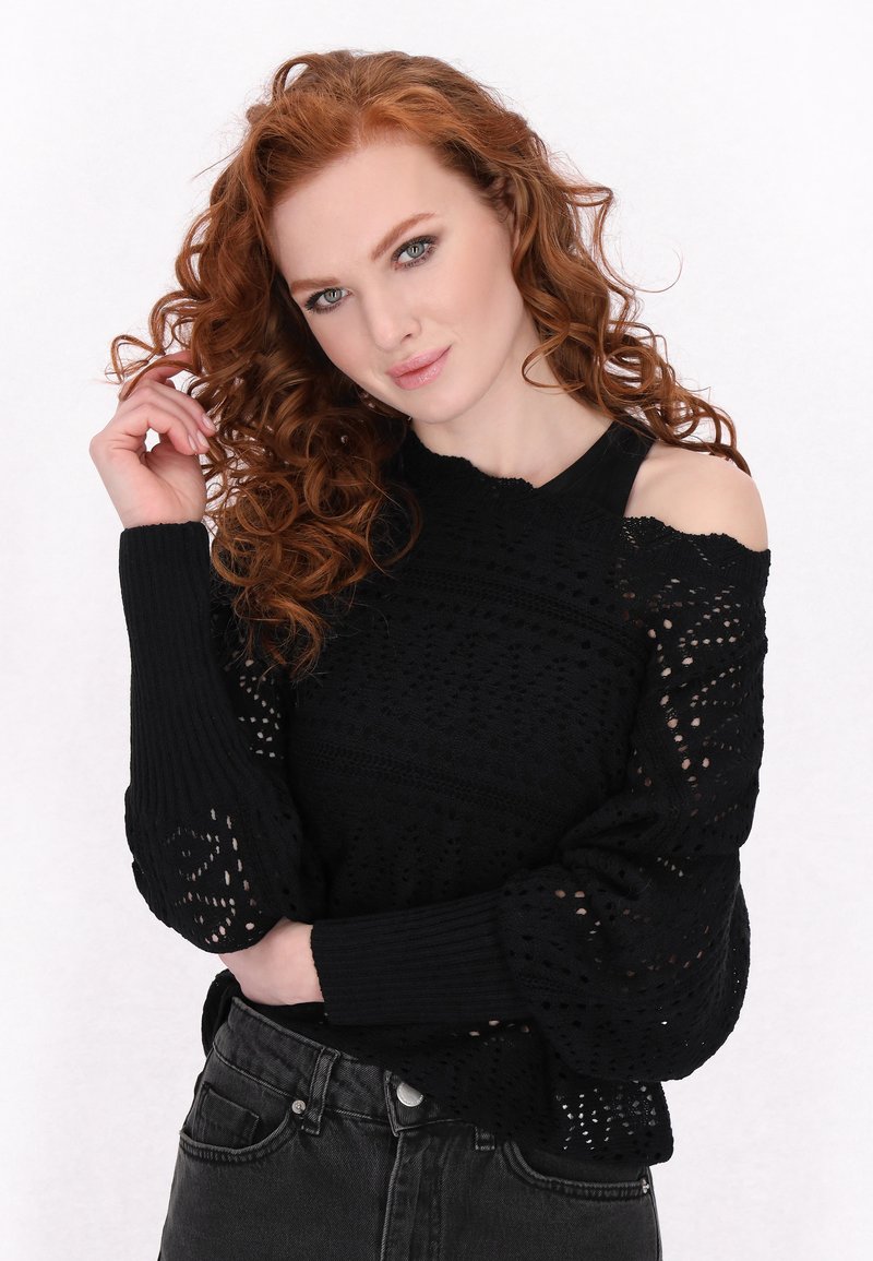Pull en maille noire avec un design en tricot ouvert, des manches larges et une coupe décolletée. Associé à un jean sombre.