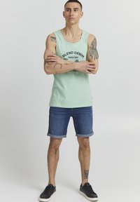Mint zelena bezrukava majica s grafikom "BLEND DENIM", uparena s trapericama koje su na rubovima zavrnute i crnim tenisicama.