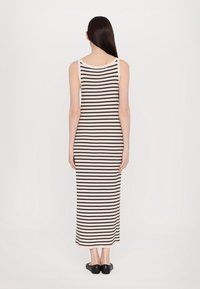 Robe tricotée rayée en crème et noir, sans manches, longueur genou, texture côtelée, avec un col rond et des fentes latérales. Chaussures noires.