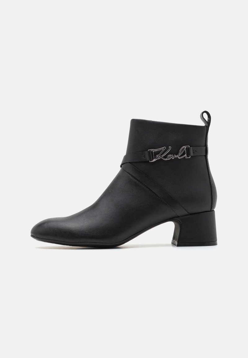 Schwarze Lederstiefelette mit spitzer Zehe, kurzem Blockabsatz und dekorativem Riemen mit metallicfarbenem "Karl"-Logo. Glatte Textur.