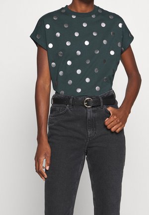 Donkergroen T-shirt met korte mouwen en zilveren stippen, gecombineerd met hoge zwarte jeans en een zwarte riem met een ronde gesp.