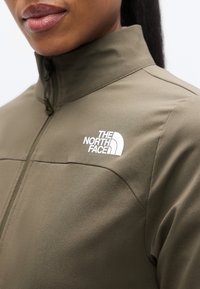 Πράσινο-ελιάς μπουφάν με ψηλό γιακά, κλείσιμο με φερμουάρ και το λογότυπο The North Face σε λευκό στο στήθος. Μαλακό, υφαντό ύφασμα.