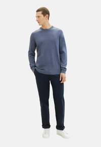 Pulover din lână albastră cu guler rotund, mâneci lungi, asortat cu pantaloni negri închis și adidași albi. Design simplu și clasic, cu o croială confortabilă.