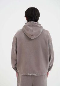 Felpa oversize grigio chiaro con tasca a marsupio, dotata di polsini a coste, cappuccio con lacci e logo ricamato all'orlo.