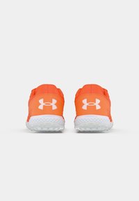 Para jasnopomarańczowych butów biegowych Under Armour widziana z tyłu na białym tle.