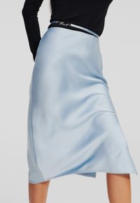 Jupe midi en satin bleu clair avec une texture lisse, présentant une ceinture contrastante et un détail en ourlet festonné.