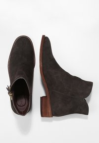 Mörkgrå mocka ankelstövlar med spetsig tå, sidogångjärn och en låg, staplad träklack. Synlig söm längs kanten.