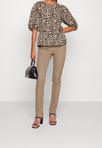 Leopardmönstrad topp med puffärmar och peplummidja, kombinerad med avsmalnande beige byxor och svarta remsandaler, håller en liten svart handväska.