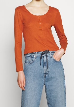 Haut à manches longues côtelé en rouille avec un décolleté en scoop et une patte de boutonnage à trois boutons, associé à un jean taille haute bleu clair avec cordon de serrage.