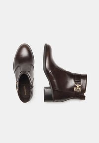 Stivaletti in pelle marrone alla caviglia con punta rotonda, tacco medio, cerniera laterale e dettaglio decorativo della fibbia. Texture liscia e design elegante.