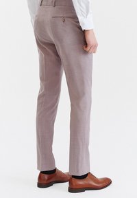 Jasnofioletowe spodnie w slim fit, z tylną kieszenią i brązowymi skórzanymi butami. Gładka tekstura, przemyślany krój.