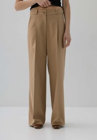 Beżowe spodnie wielką nogawką z zakładkami, wykonane z lekkiego materiału. Posiadają zapięcie na guziki w talii oraz dyskretne kieszenie z przodu.
