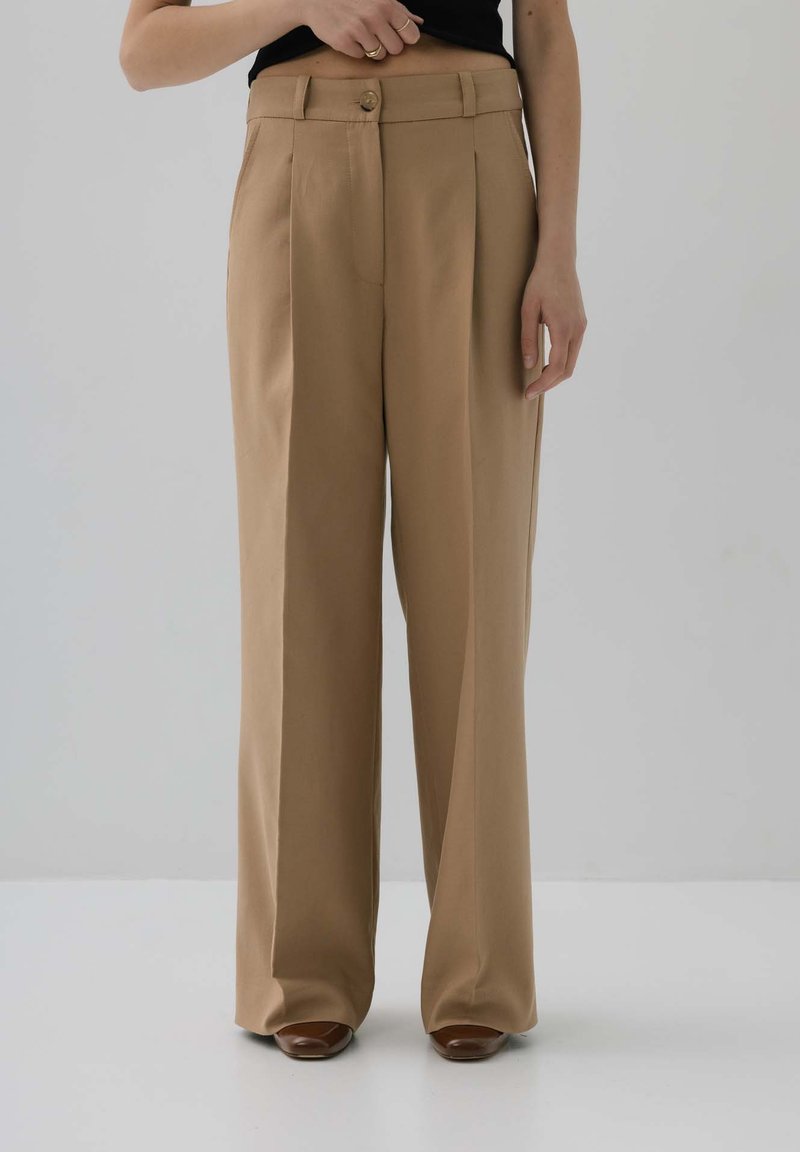 Beżowe spodnie wielką nogawką z zakładkami, wykonane z lekkiego materiału. Posiadają zapięcie na guziki w talii oraz dyskretne kieszenie z przodu.