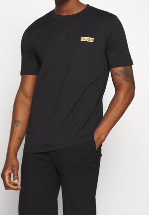 Czarna bawełniana koszulka z okrągłym dekoltem i krótkimi rękawami, z małym żółtym prostokątnym logo z napisem "HUGO." Gładka tekstura tkaniny.