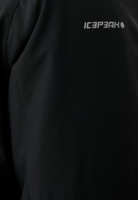 Veste noire avec une texture lisse et mate. Le nom de la marque "ICEPEAK" est imprimé en argent sur la partie supérieure. Le design comprend des coutures élégantes.