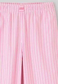 Pantalons de pyjama à rayures roses avec une taille froncée et une étiquette indiquant "CRÉÉ POUR VOTRE CONFORT". Les rayures sont blanches et rose clair.