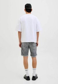Witte oversized t-shirt, grijze opgerolde denim shorts, zwarte pet, zwarte schoenen en witte sokken met logo. Casual ontwerp met een ontspannen pasvorm.