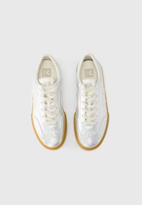 Ασημί δερμάτινα αθλητικά παπούτσια με λεία υφή, με μπεζ κορδόνια, σόλες από καουτσούκ και διακριτικές ραφές.
