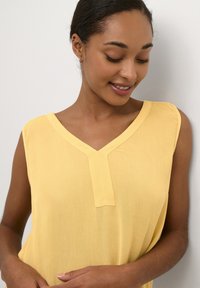 Yellow sleeveless blouse with a V-neck and textured fabric. Features a panel detail at the neckline and soft, flowing shape.