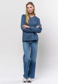 Zils kokvilnas sporta krekls ar V-veida izgriezumu, garām piedurknēm un mazu izšūtu logotipu. Kombinēts ar gaiši ziliem plaša piegriezuma džinsiem un sporta apaviem.