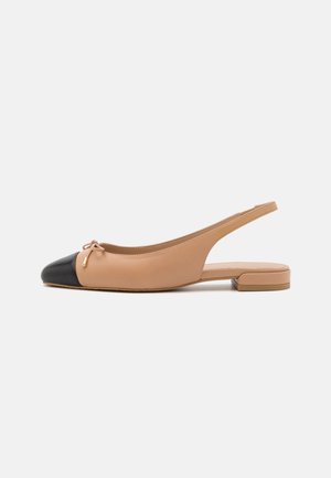 Ballerines à dos ouvert en cuir beige avec un bout noir. Présentent un accent de nœud et un petit talon carré pour plus de soutien. Fini texturé et lisse.