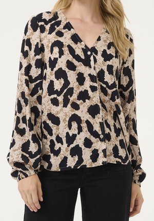 Blouse beige à imprimé léopard noir et marron, manches longues bouffantes, boutonnée devant, portée avec un pantalon noir.