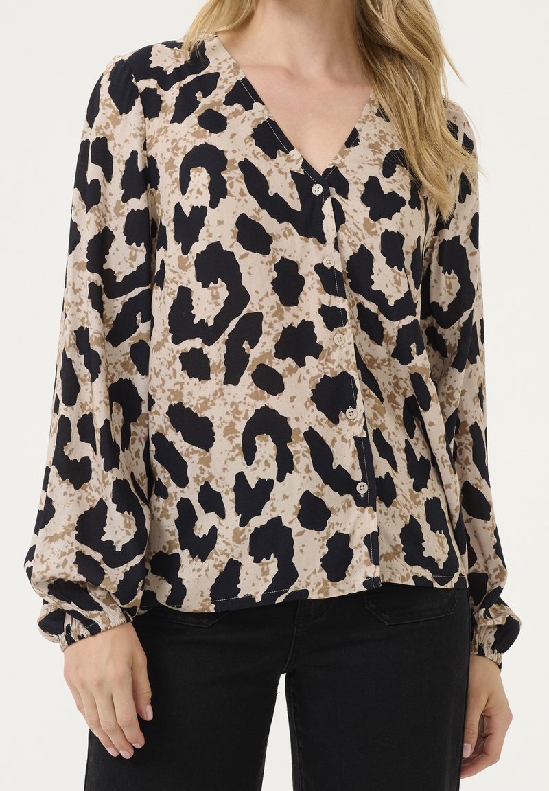 Blouse beige à imprimé léopard noir et marron, manches longues bouffantes, boutonnée devant, portée avec un pantalon noir.
