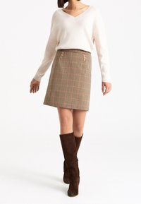 Béžový žebrovaný svetr, hnědá nohavicová sukně se vzorem psa zepředu s knoflíky a hnědé semišové kozačky nad kolena. Měkká textura, střih na míru.