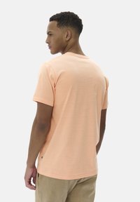 T-shirt pour homme à manches courtes en pêche clair, arborant un motif texturé à rayures et un col rond, associé à un pantalon beige.