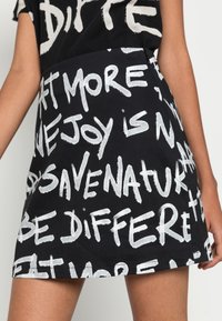 Vestido de tela negra con un patrón de frases escritas a mano en blanco. Tiene una silueta ajustada y un dobladillo recto, con mangas cortas.