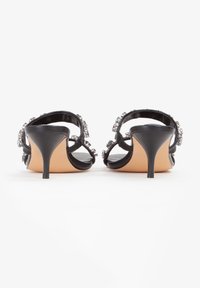 Le sandali neri con tacco alto presentano una parte superiore lucida, decorata con gemme trasparenti sulle cinghie e un sottile tacco a stiletto.